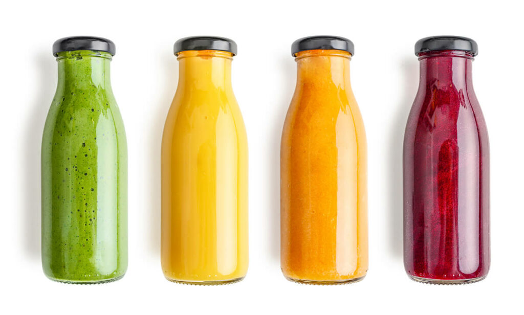 Green, yellow, orange and red smoothie in glass bottles